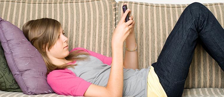 Girls laying on a couch using a cell phone